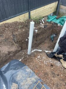 PVC plumbing pipes positioned in a dug trench during outdoor construction work.